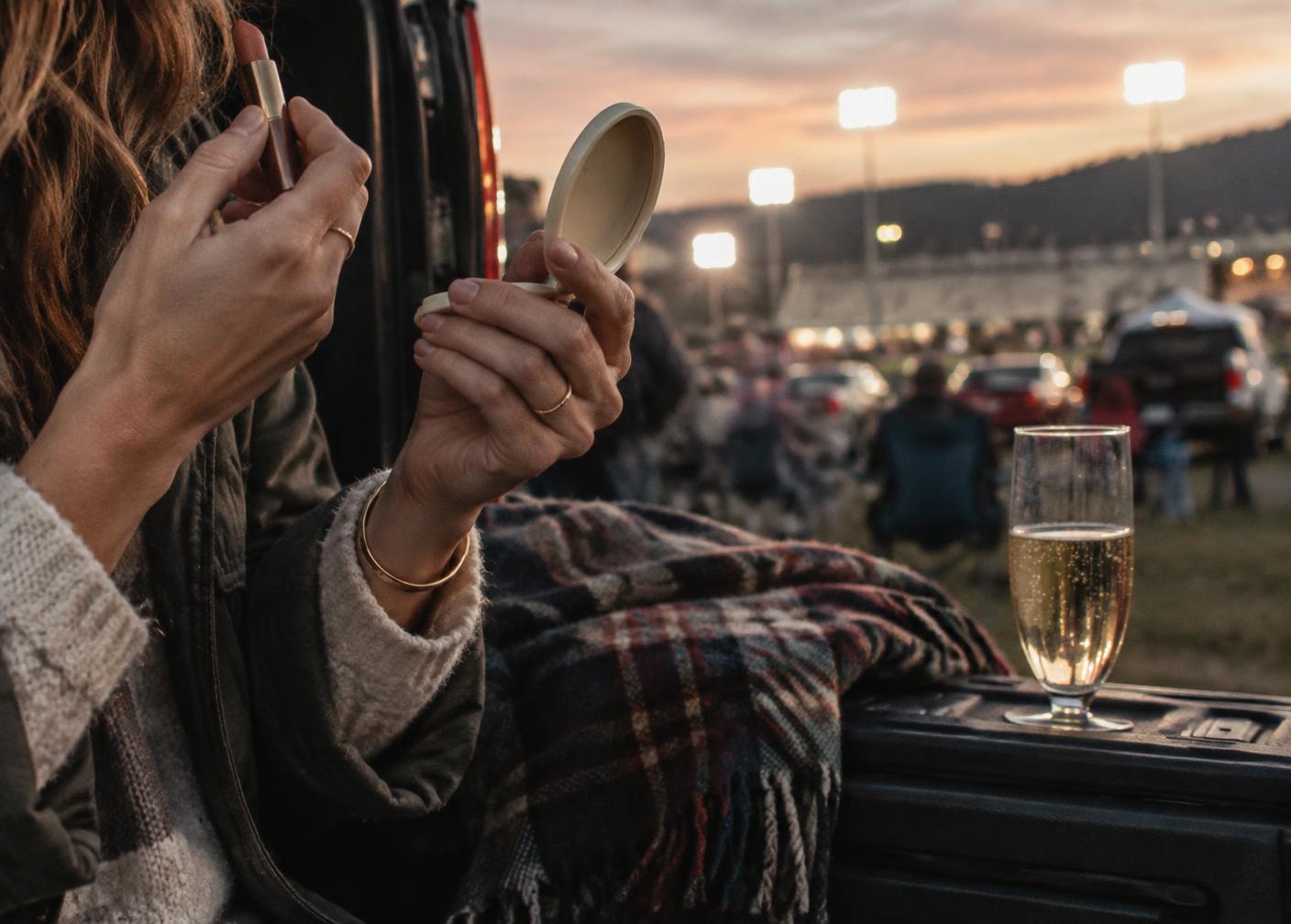 Guest touching up lipstick at the tailgate at dusk